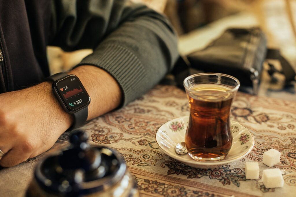 ساعت هوشمند روی مچ دست همراه با استکان چای در فضایی گرم و خانگی